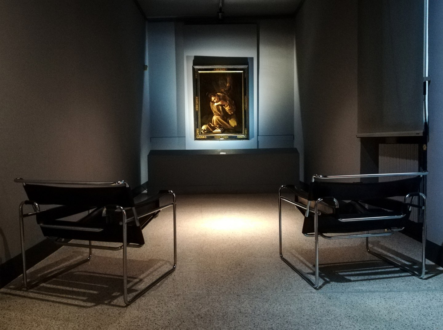 Sala del Caravaggio, una piccola stanza intima con la tela illuminata sullo sfondo. in primo piano le sedute per i visitatori